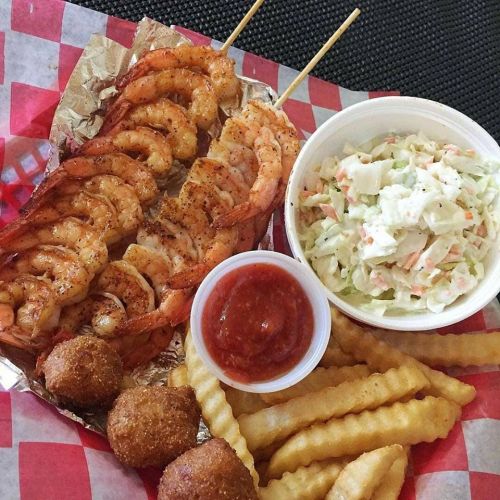 Grilled shrimp skewers with coleslaw, crinkle fries, and hushpuppies served with a side of dipping sauce.