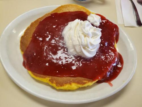 A plate of pancakes topped with strawberry sauce and whipped cream.