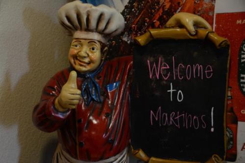 A cheerful chef statue giving a thumbs up next to a chalkboard sign that says "Welcome to Martino's!"