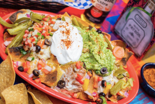 A vibrant plate of nachos topped with guacamole, sour cream, jalapeños, olives, and fresh pico de gallo.