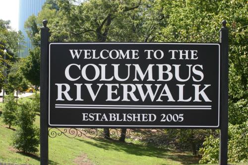 Sign welcoming visitors to the Columbus Riverwalk, established in 2005, surrounded by greenery.