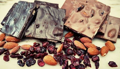 A variety of chocolate bars arranged with almonds and dried cranberries scattered around them.