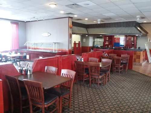 Interior of a restaurant featuring wooden tables and chairs, red booths, and a buffet area in the background.
