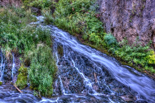A serene waterfall cascading over rocks, surrounded by lush green vegetation and wildflowers.