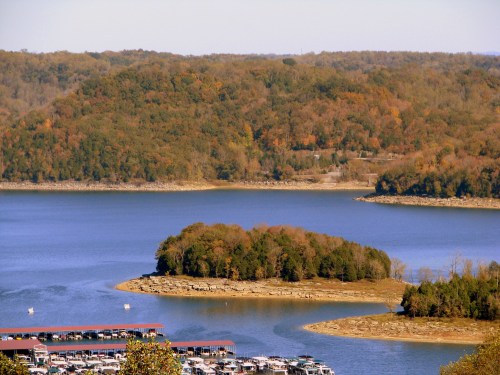 A scenic view of a lake surrounded by autumn-colored trees and a marina with boats.