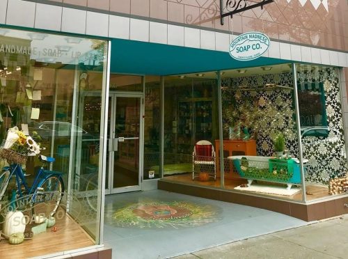 A storefront of Mountain Made Soap Co., featuring a colorful entrance and decorative window displays.