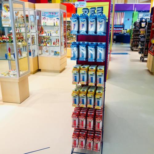 A display rack filled with various products in a colorful store, surrounded by shelves of toys and merchandise.