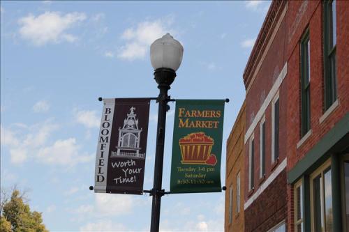 Two banners on a lamp post: one for Bloomfield and another advertising the Farmers Market schedule.