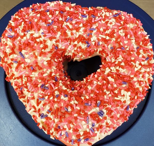 A heart-shaped donut covered in pink icing and colorful sprinkles on a blue plate.