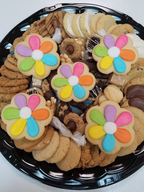 A platter of assorted cookies, including flower-shaped cookies with colorful icing and various chocolate treats.