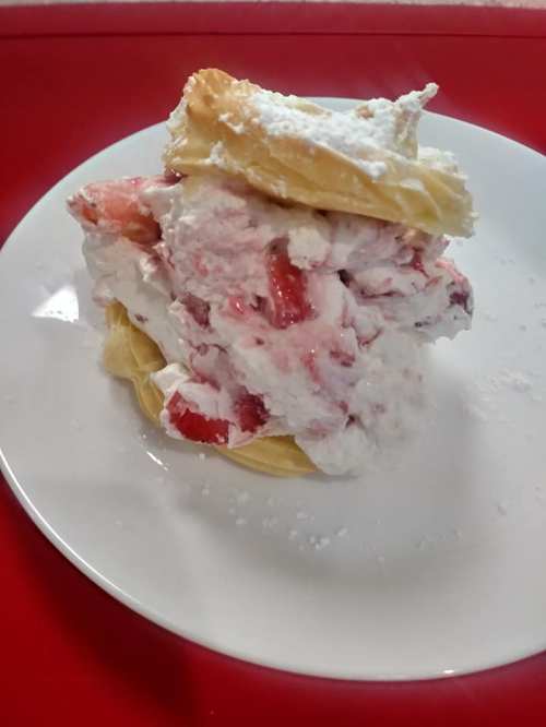 A layered dessert with flaky pastry, whipped cream, and fresh strawberries, dusted with powdered sugar on a white plate.