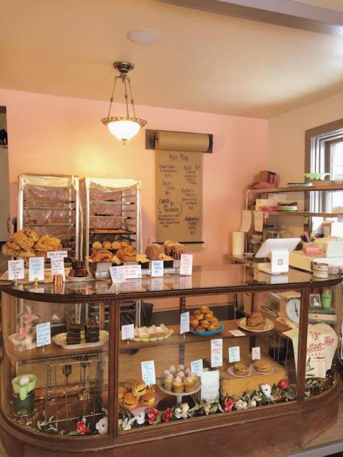 A cozy bakery display featuring various pastries, muffins, and cupcakes behind a glass counter with charming decor.