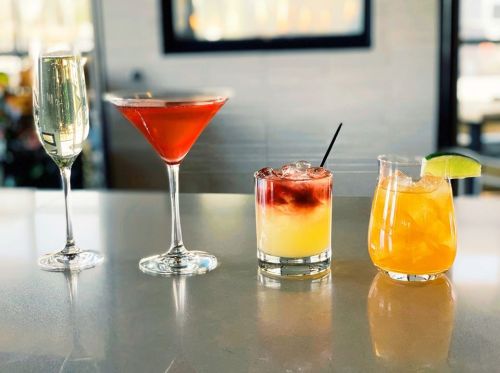 Four colorful cocktails on a bar counter: a champagne flute, a martini, a layered drink, and a citrus cocktail.