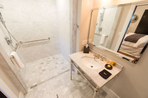 Modern bathroom featuring a marble shower, sink with elegant fixtures, and a large mirror. Bright and spacious design.