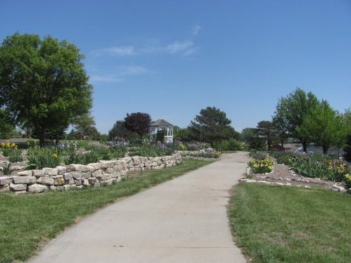 A paved path lined with flowers and shrubs leads to a gazebo under a clear blue sky.