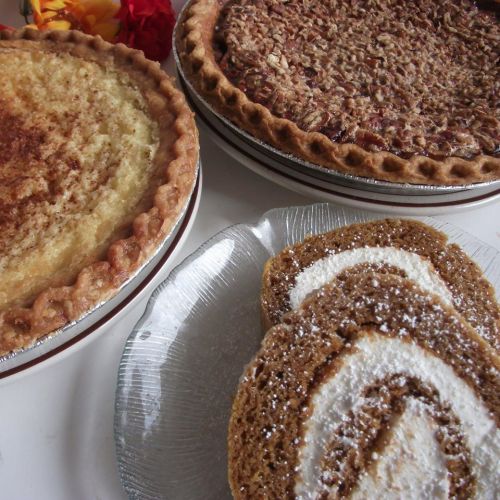 Three delicious pies: a pecan pie, a coconut cream pie, and a pumpkin roll with cream filling, all beautifully presented.