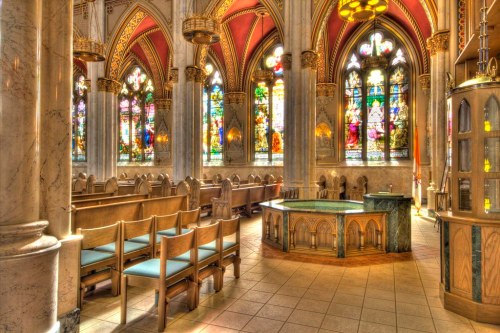 Interior of a grand church featuring ornate arches, colorful stained glass windows, and wooden pews.