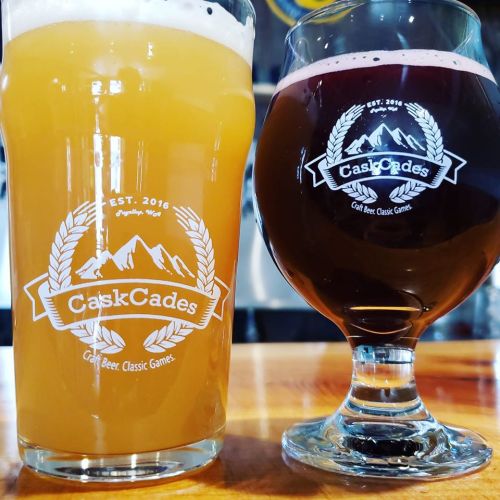 Two craft beer glasses on a wooden table, one filled with a light golden beer and the other with a dark red beer.