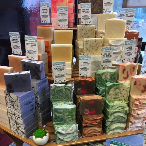 A colorful display of various handmade soaps arranged on wooden shelves, featuring different shapes and scents.