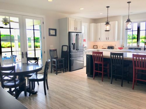 Bright kitchen with white cabinets, a large island, and a dining table. Large windows let in natural light.
