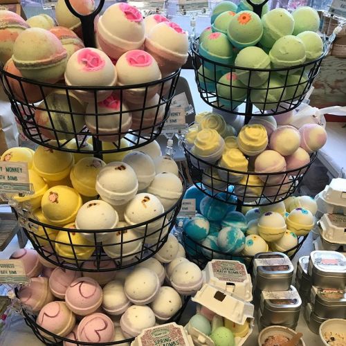 A display of colorful bath bombs in various shapes and sizes, arranged in wire baskets and on a table.