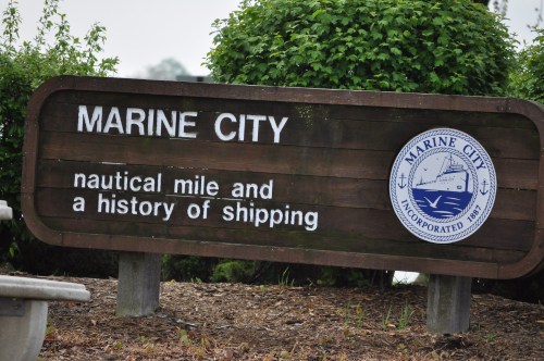 Sign for Marine City, highlighting its nautical mile and history of shipping, with a logo and greenery in the background.