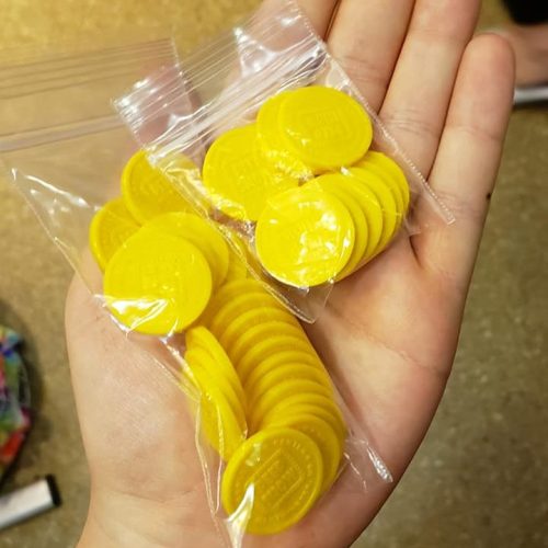 A hand holding two clear bags filled with yellow circular tokens.