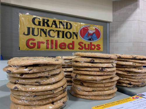 Stacks of wrapped chocolate chip cookies in front of a "Grand Junction Grilled Subs" banner.