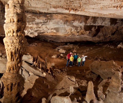 A group of people stands in a large cave, surrounded by rock formations and stalactites hanging from the ceiling.