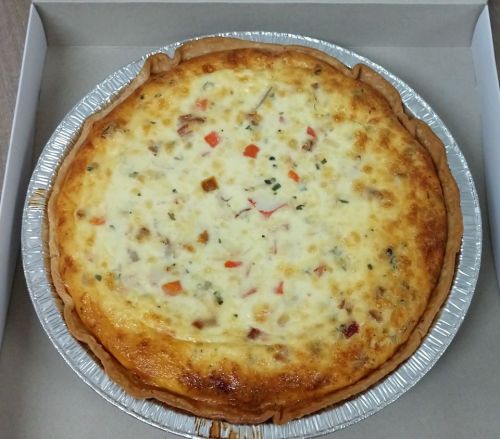A freshly baked quiche in a silver pie dish, featuring a golden crust and a creamy filling with vegetables and meat.