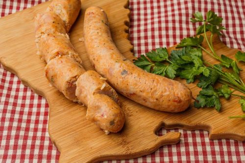 Two uncooked sausages on a wooden cutting board, accompanied by fresh parsley, on a red and white checkered tablecloth.