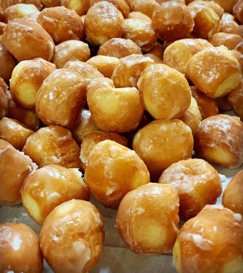 A close-up of a pile of glazed doughnut holes, golden brown and shiny, arranged closely together.