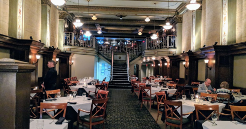 Elegant restaurant interior with wooden accents, tables set for dining, and a staircase leading to an upper level.