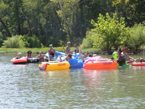 A group of people relaxes on colorful inflatable rafts in a calm river surrounded by lush greenery.