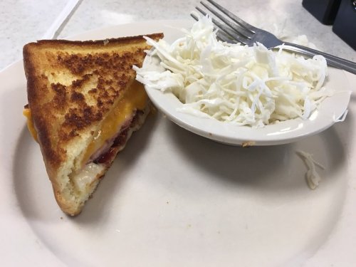 A toasted sandwich with melted cheese and a side of shredded cabbage on a plate.