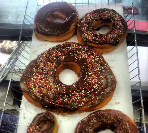 A display of large donuts, two topped with chocolate icing and colorful sprinkles, and one with a chocolate glaze.