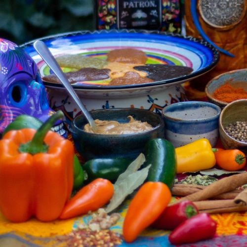 A colorful spread of spices, peppers, and bowls, with a decorative plate and vibrant skulls in the background.