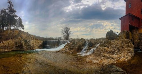 A scenic view of a waterfall cascading over rocky terrain, with a cloudy sky and trees in the background.