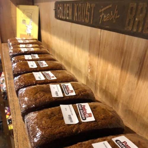 Loaves of bread neatly arranged on a wooden shelf, with labels visible on each loaf.