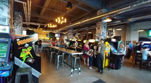 A lively arcade with vintage games, patrons enjoying the atmosphere, and colorful decor in a spacious setting.