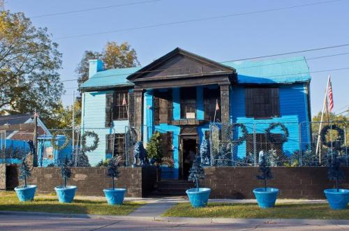 A striking blue house with black accents, surrounded by blue planters and a decorative fence.