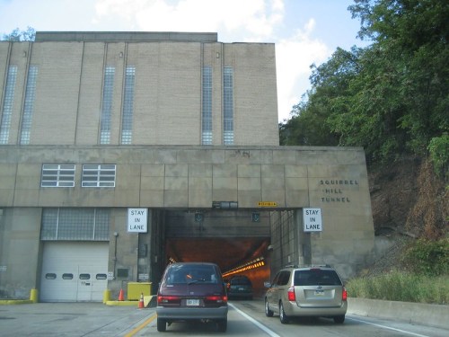 Cars entering the Squirrel Hill Tunnel, with signs indicating to stay in lane, surrounded by a rocky hillside.