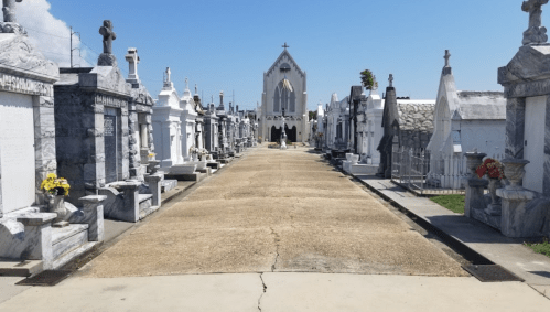 A cemetery pathway lined with tombstones, leading to a church under a clear blue sky.