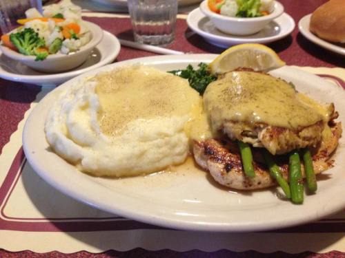A plate of grilled chicken topped with sauce, asparagus, and a lemon wedge, served with mashed potatoes and a side salad.