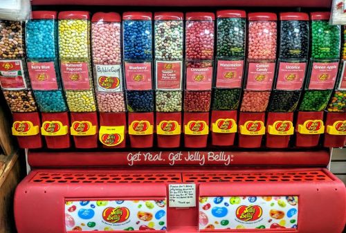 A colorful display of Jelly Belly jelly beans in various flavors, arranged in clear dispensers on a red background.