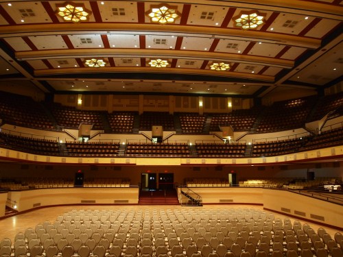 A spacious auditorium with rows of empty chairs and decorative ceiling lights, ready for an event.