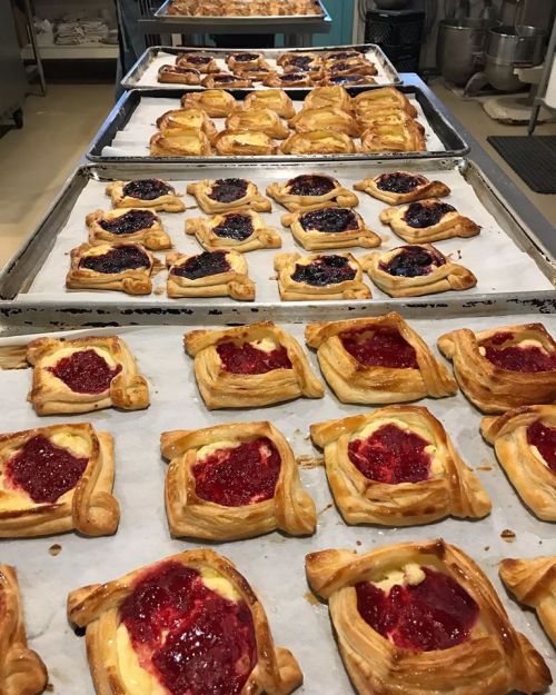 Trays of freshly baked pastries with fruit fillings, arranged neatly on parchment paper in a kitchen.