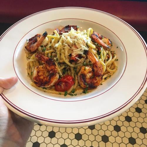 A plate of pasta with shrimp, cherry tomatoes, and herbs, garnished with grated cheese, held in a hand.