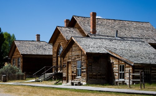 Historic wooden buildings with sloped roofs under a clear blue sky, surrounded by grassy land.