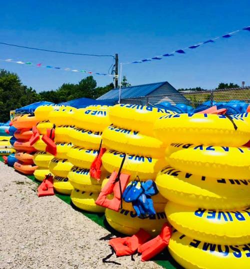 A stack of bright yellow inflatable tubes and orange life jackets at a water park, with blue skies in the background.